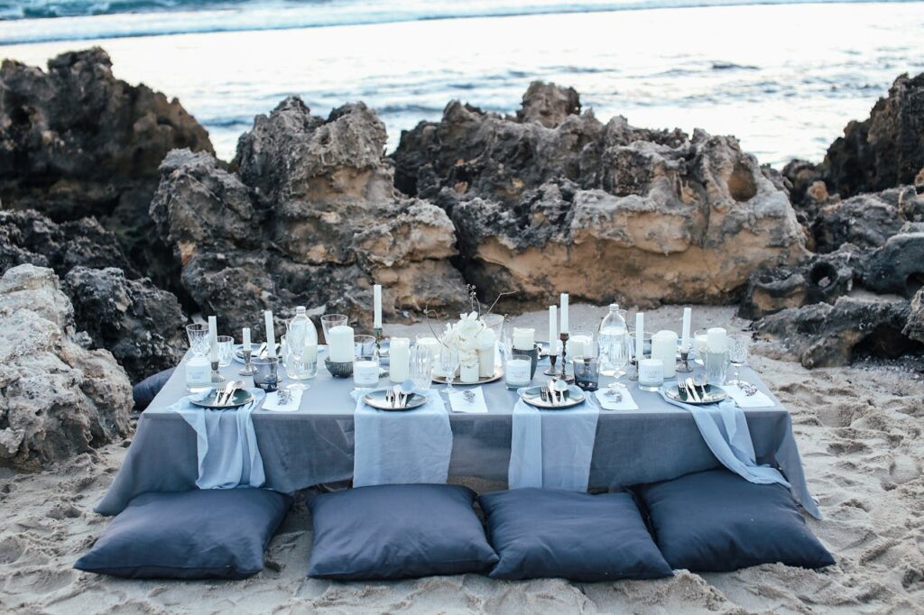 A beautifully set table with candles and cushions by the beach, perfect for an event.